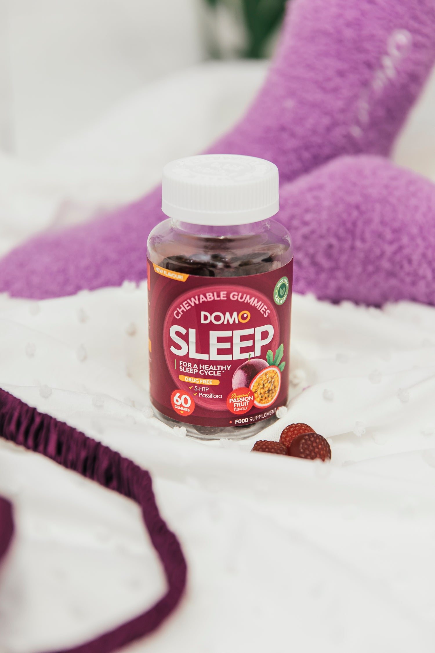 A bottle of Domo Sleep Gummies on a bed in front of pair of feet wearing purple fluffy socks. 
