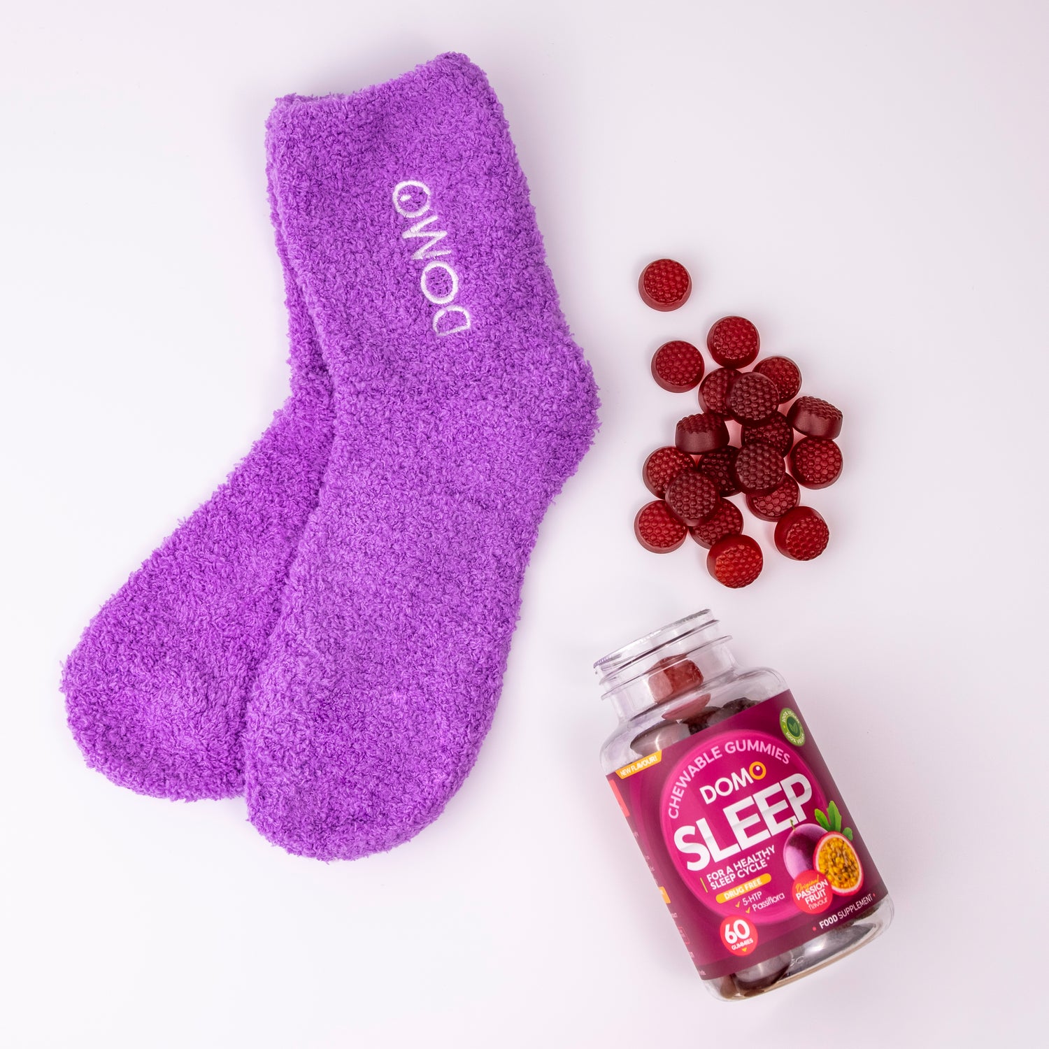 An open bottle of Domo Sleep Gummies beside a pair of purple fluffy socks. 